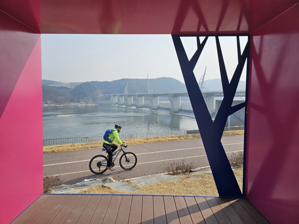 5일 오전 11시께 한 자전거 라이더가 여주 강천보 잔디밭에 만들어 놓은 포토존 속에서 강천보를 배경으로 힘차게 달리고 있다. (사진=김광섭 기자)