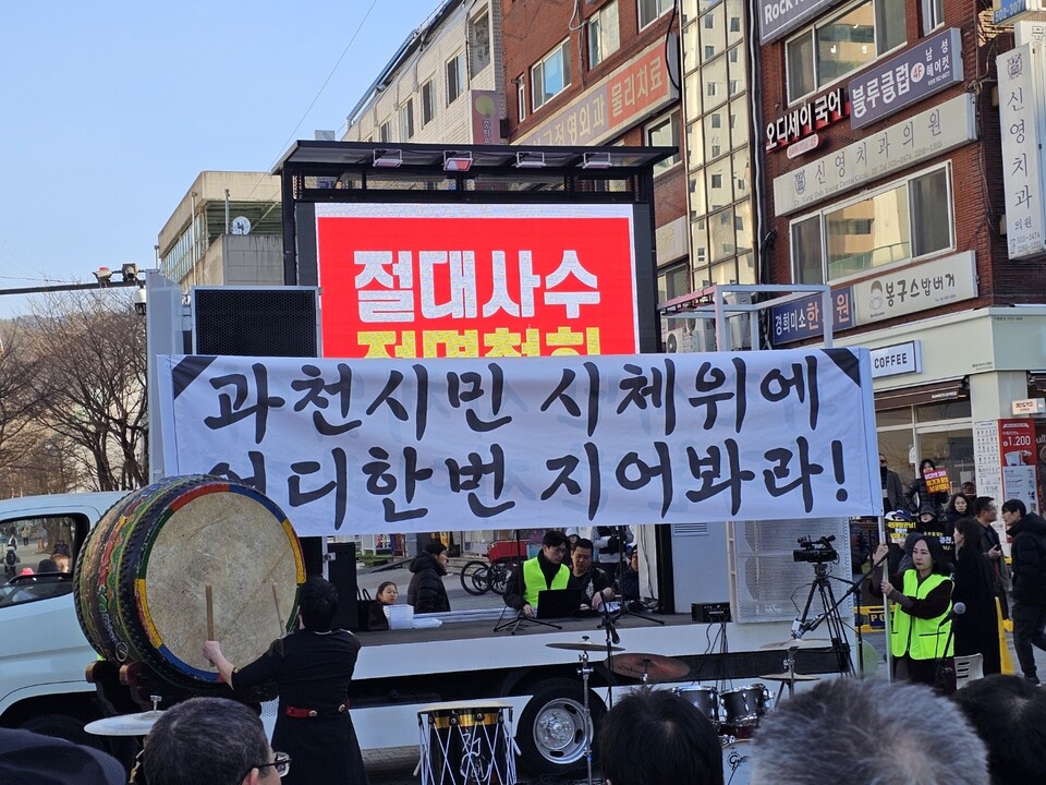 무대 전광판에는 ‘절대사수 전면철회’ 문구가 띄워졌고, 무대 앞에는 ‘과천시민 시체 위에 니 한 번 지어봐라’라고 적힌 대형 펼침막이 내걸렸다. (사진=김상현 기자)<br>