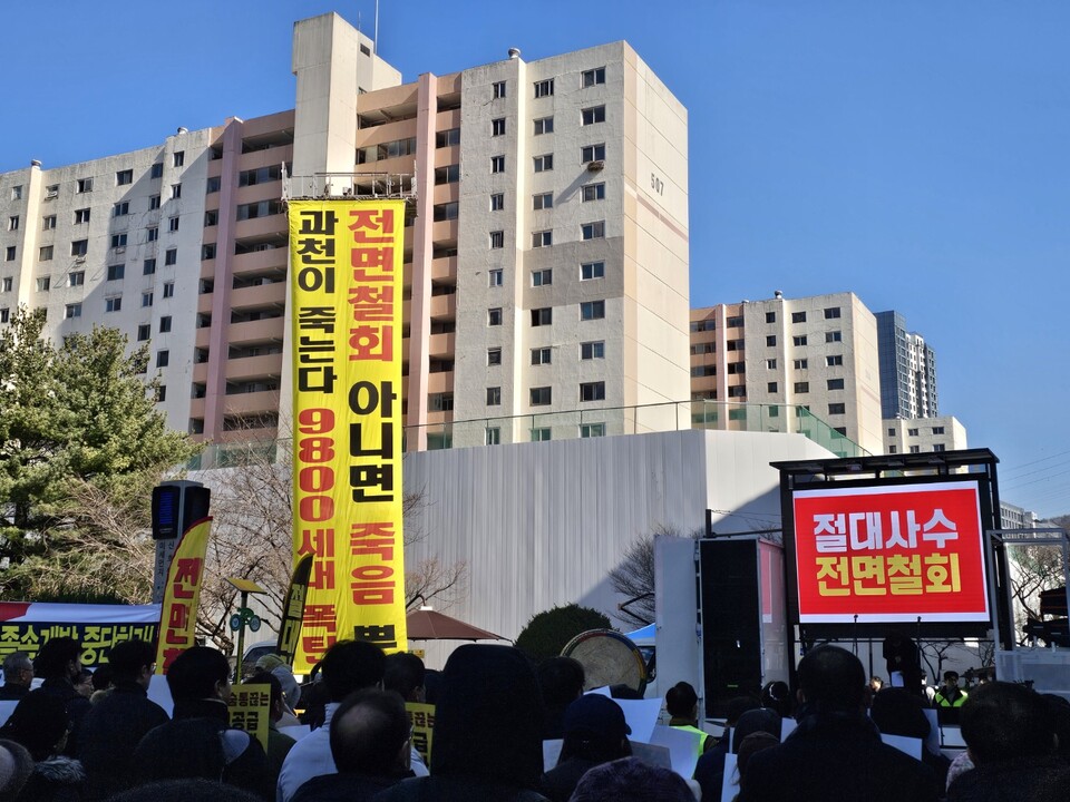 집회 현장 한편에 ‘전면철회 안 하면 죽음뿐’, ‘과천이 죽는다 9800세대 폭탄’ 등의 대형 현수막이 걸려 있다. 정부의 주택 공급 계획에 대한 지역 반발이 현장 곳곳에 드러났다. (사진=김상현 기자)<br>