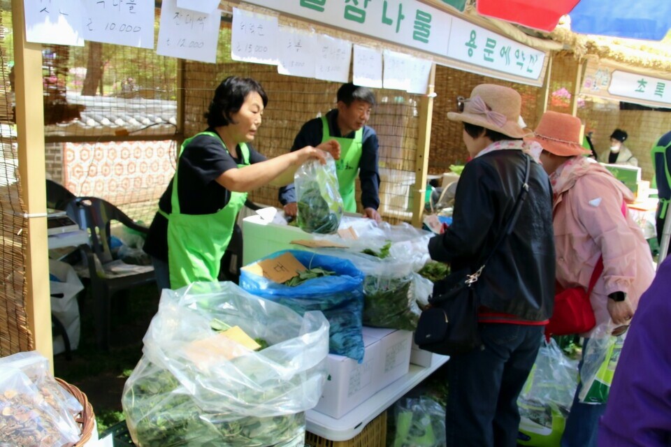 산나물 판매 부스에서 상인들이 방문객들에게 상품을 건네며 판매를 이어가고 있다.